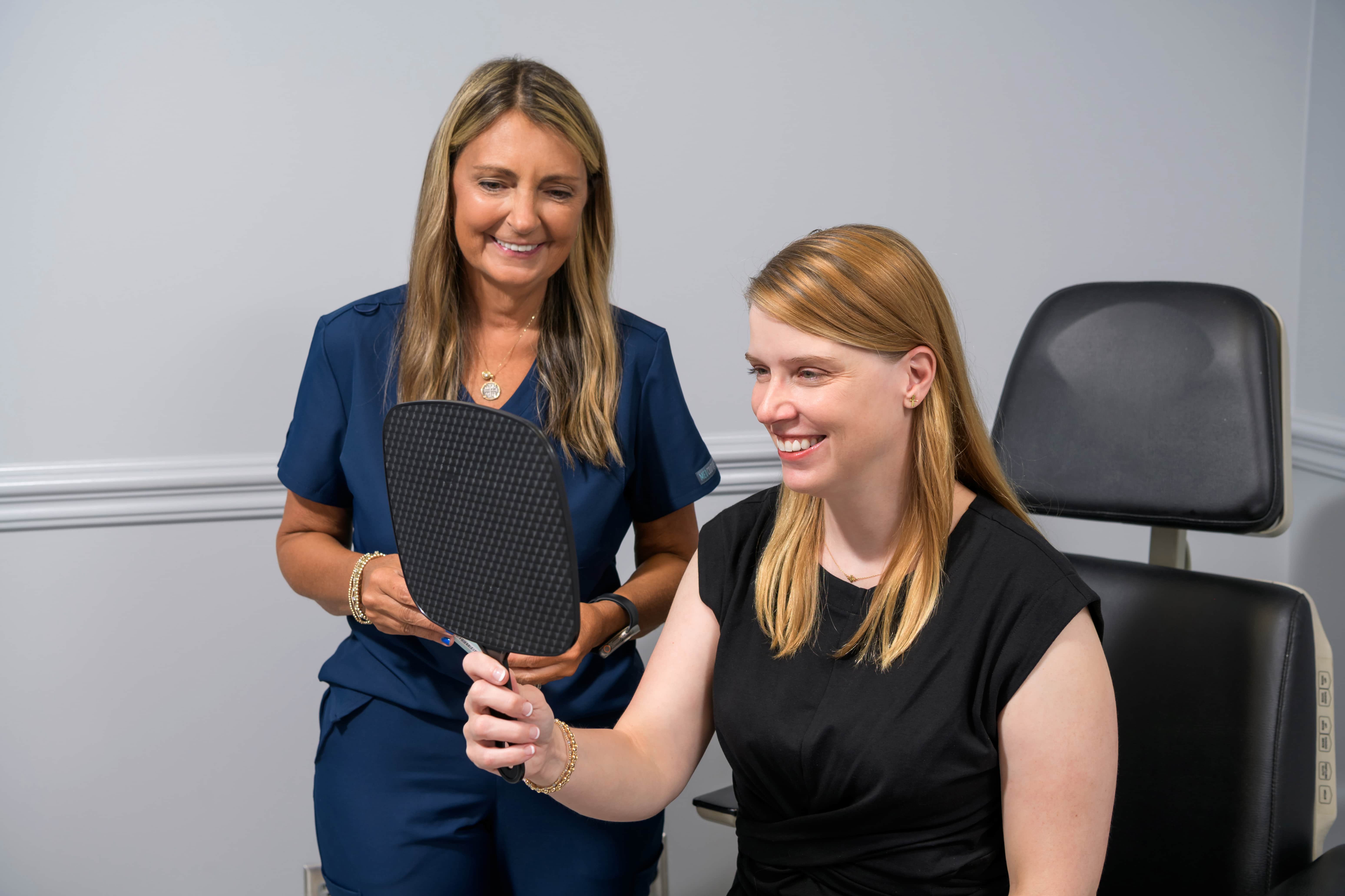 Sharon Simpson assisting a caucasian female patient who's looking at her face in a handheld mirror