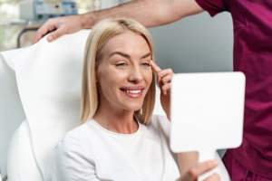 Beautiful young woman sitting in medical chair and looking in a handheld mirror.